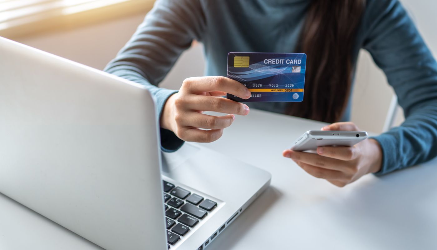 Person holding a payment card and smartphone beside a laptop