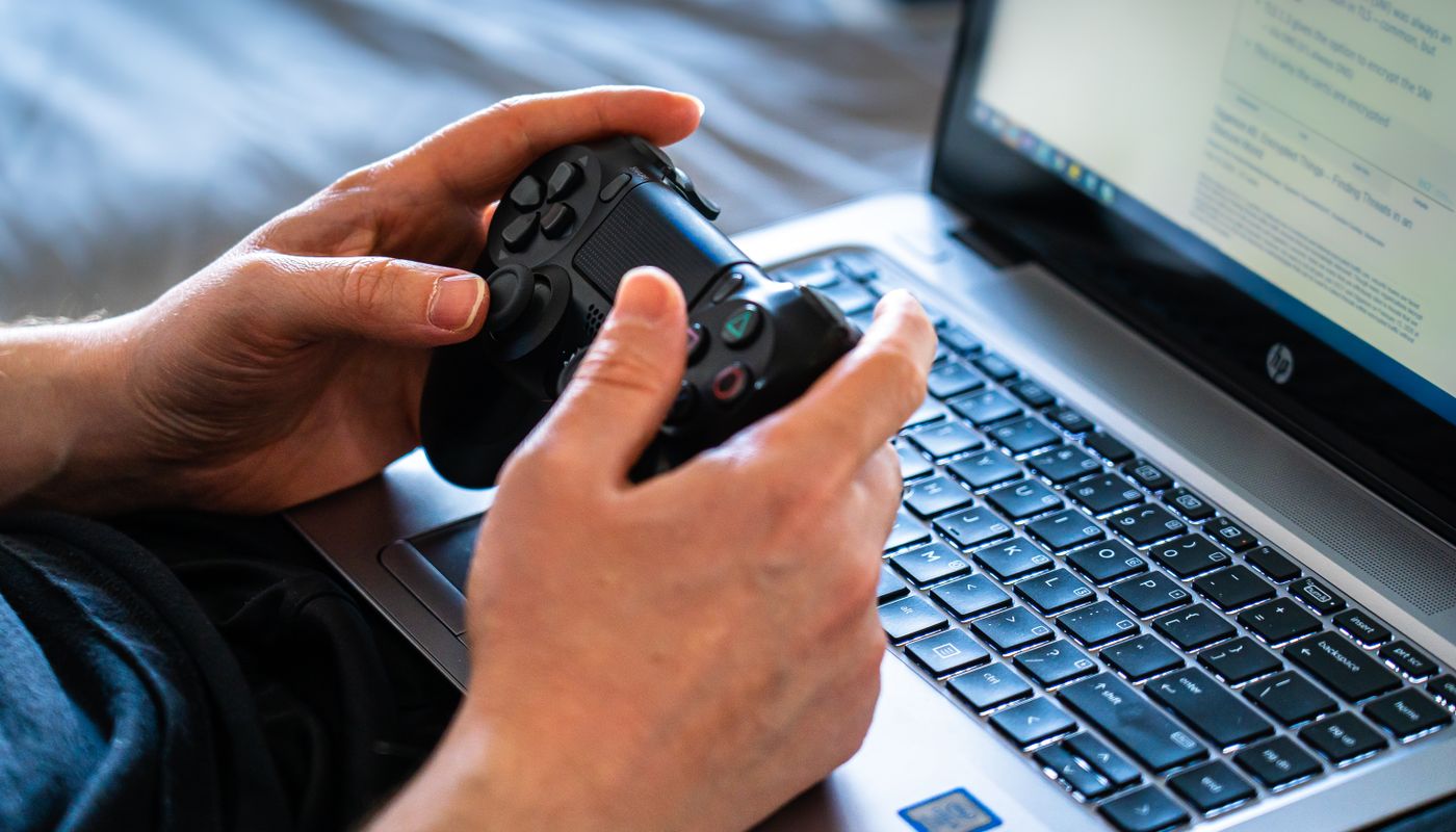 Hands holding a game controller beside a laptop
